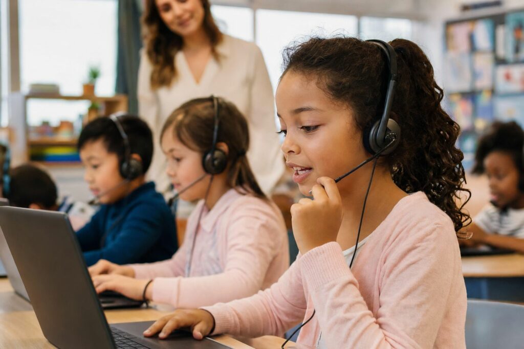 Elementary students wearing headsets at laptops during WIDA ACCESS practice test, one student speaking into the microphone